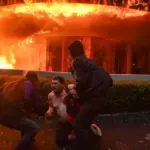 Seorang pegawai mess MPR RI dibantu peserta aksi untuk menjauh dari lokasi kebakaran saat demo